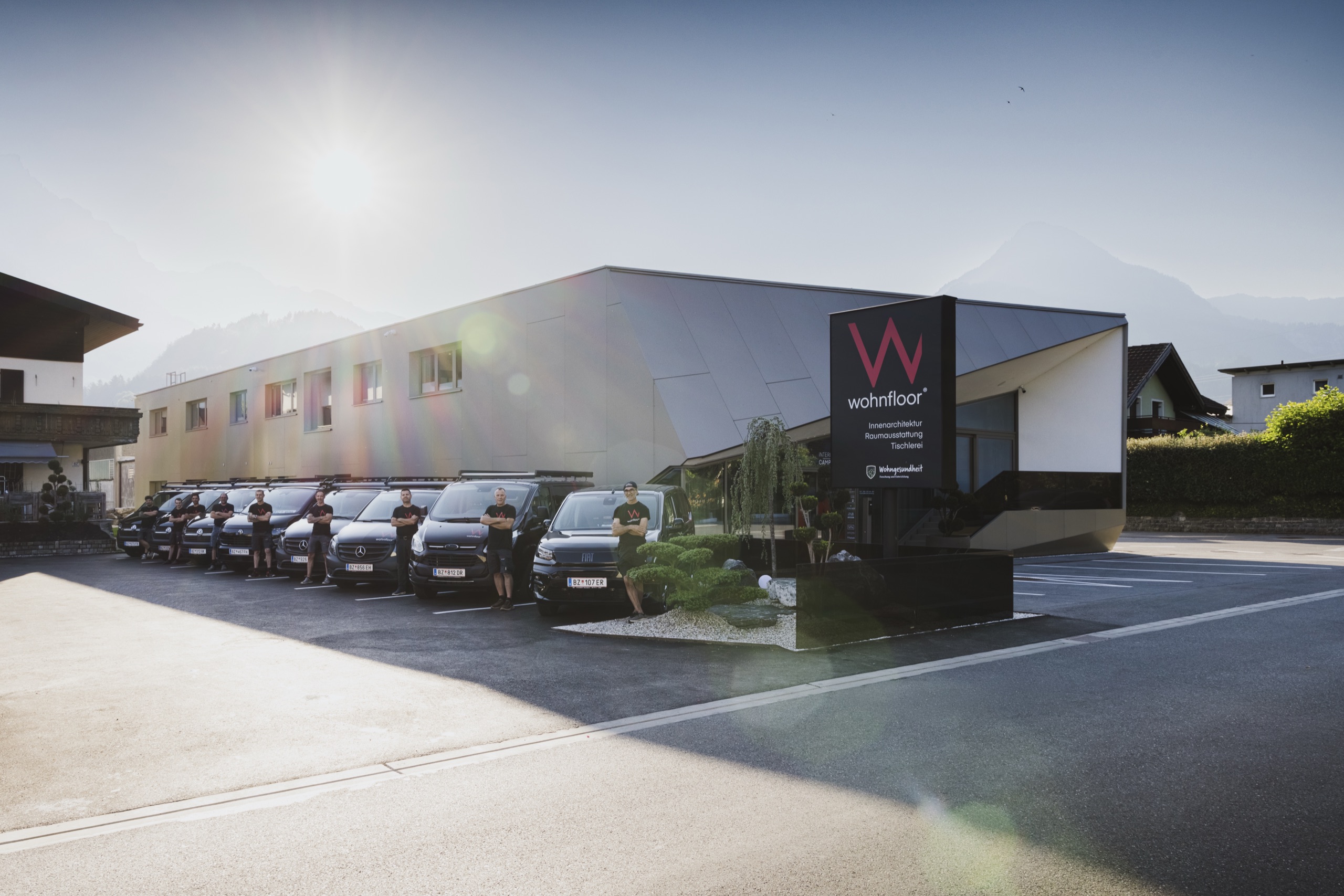 Firmengebäude von Wohnfloor in Bludenz mit Fahrzeugflotte und Team im Morgenlicht