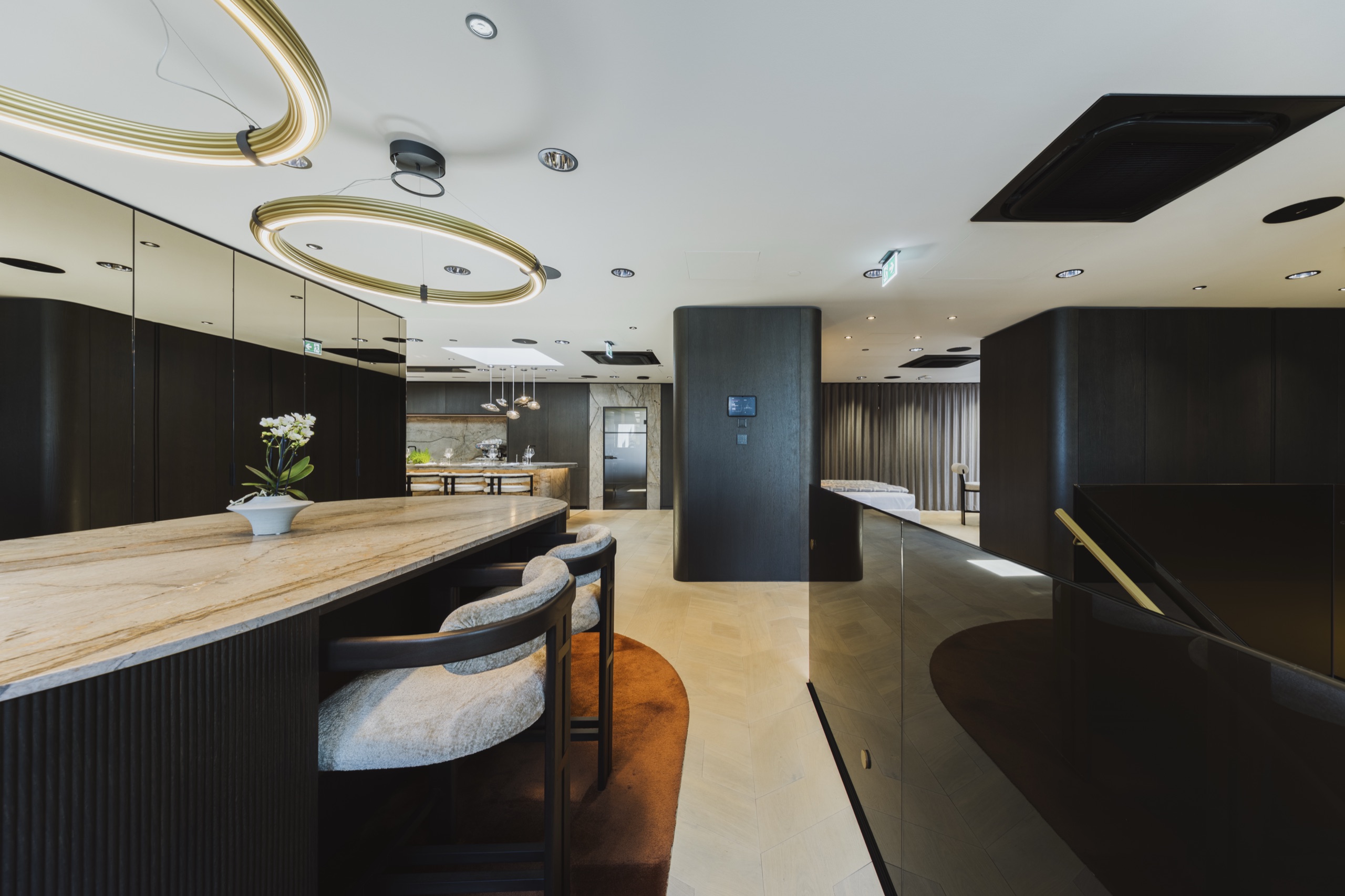 Eleganter Schauraum von Wohnfloor mit dunklen Möbeln, Naturstein-Theke und goldenen Ringleuchten